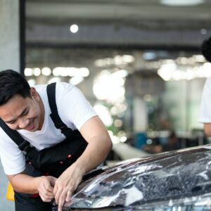 Detailing film specialist cutting and wrapping car at auto repair shop