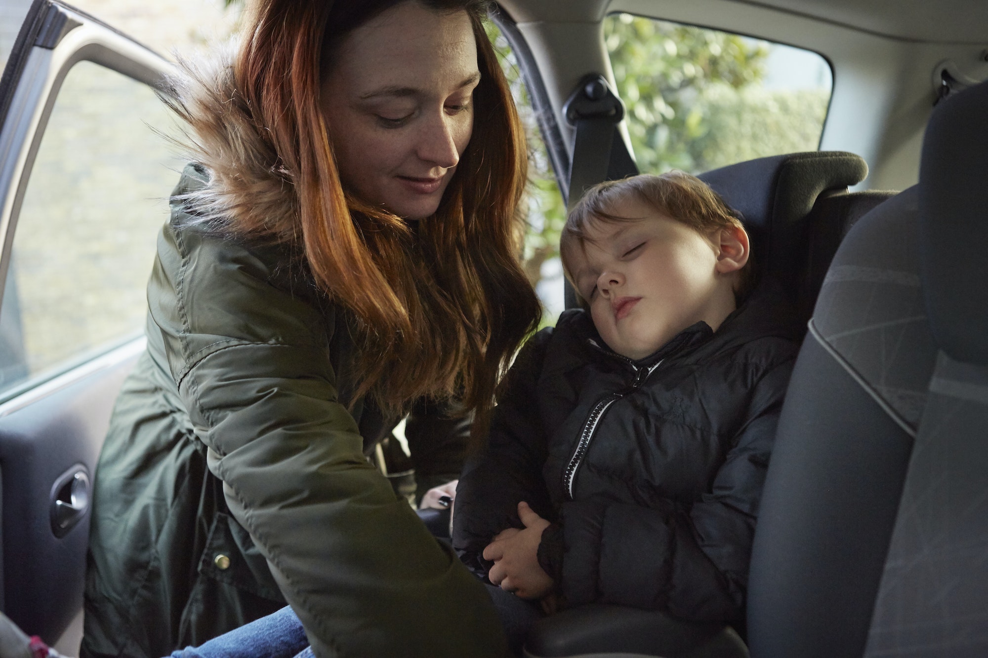 Mother removing sleeping toddler son from car backseat
