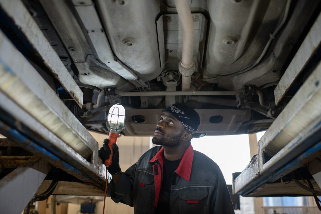 Serious young male technician with lamp checking lower part of car