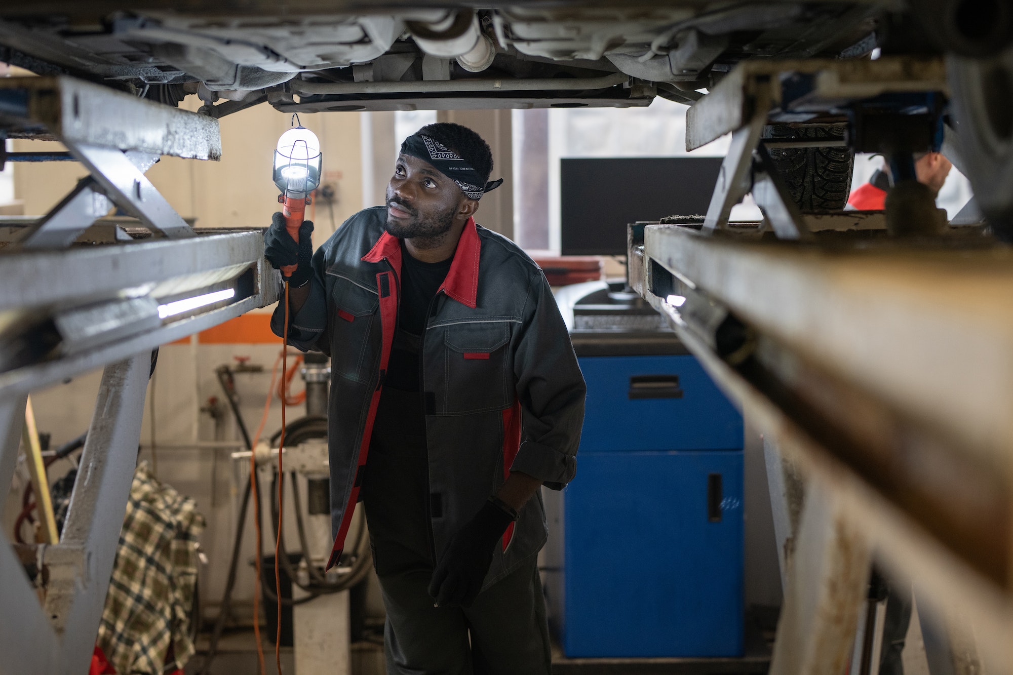 Young African man in workwear holding lamp by lower part of car