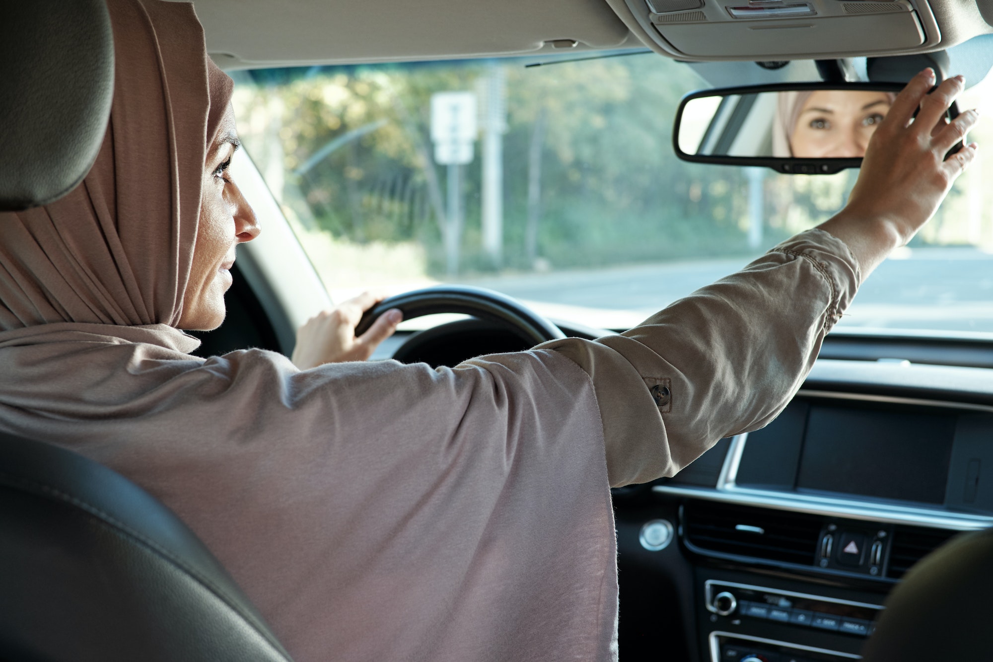 Young woman in hijab looking in mirror while driving car